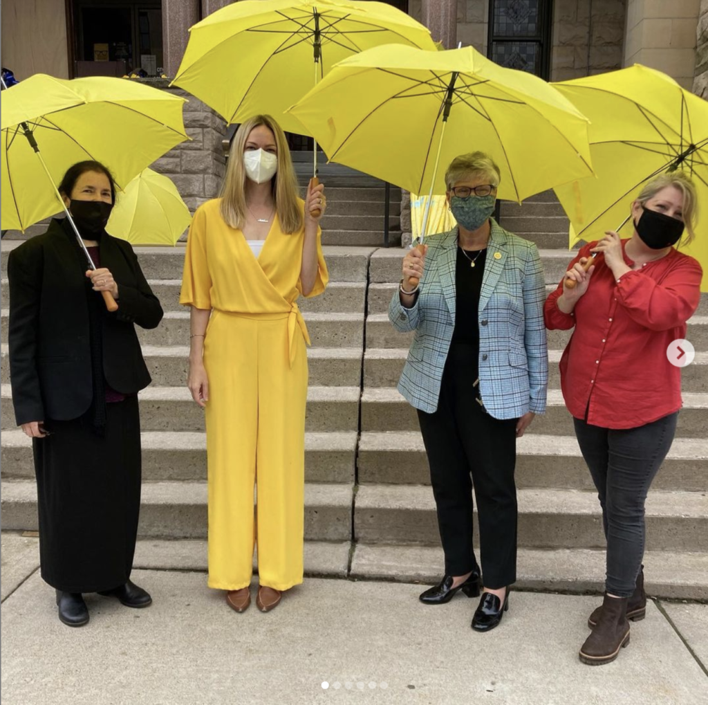 four women stand with yellow umbrellas on the courthouse steps. Glenna Lang, Mayor Cognetti, and two other guests. 